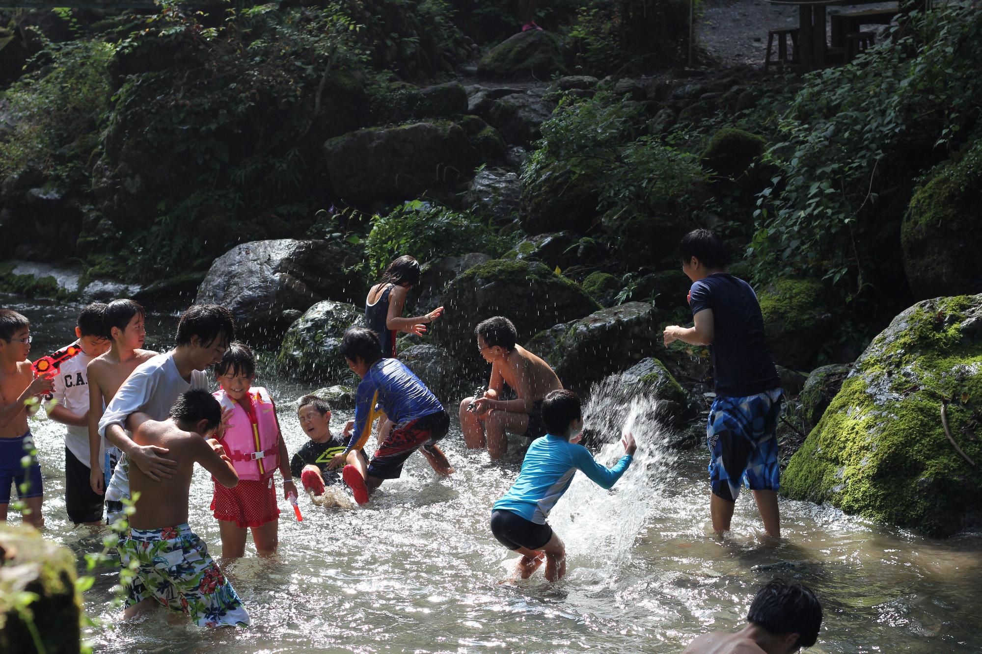 川で水着姿になり水を掛け合って遊んでいる子供たちの写真