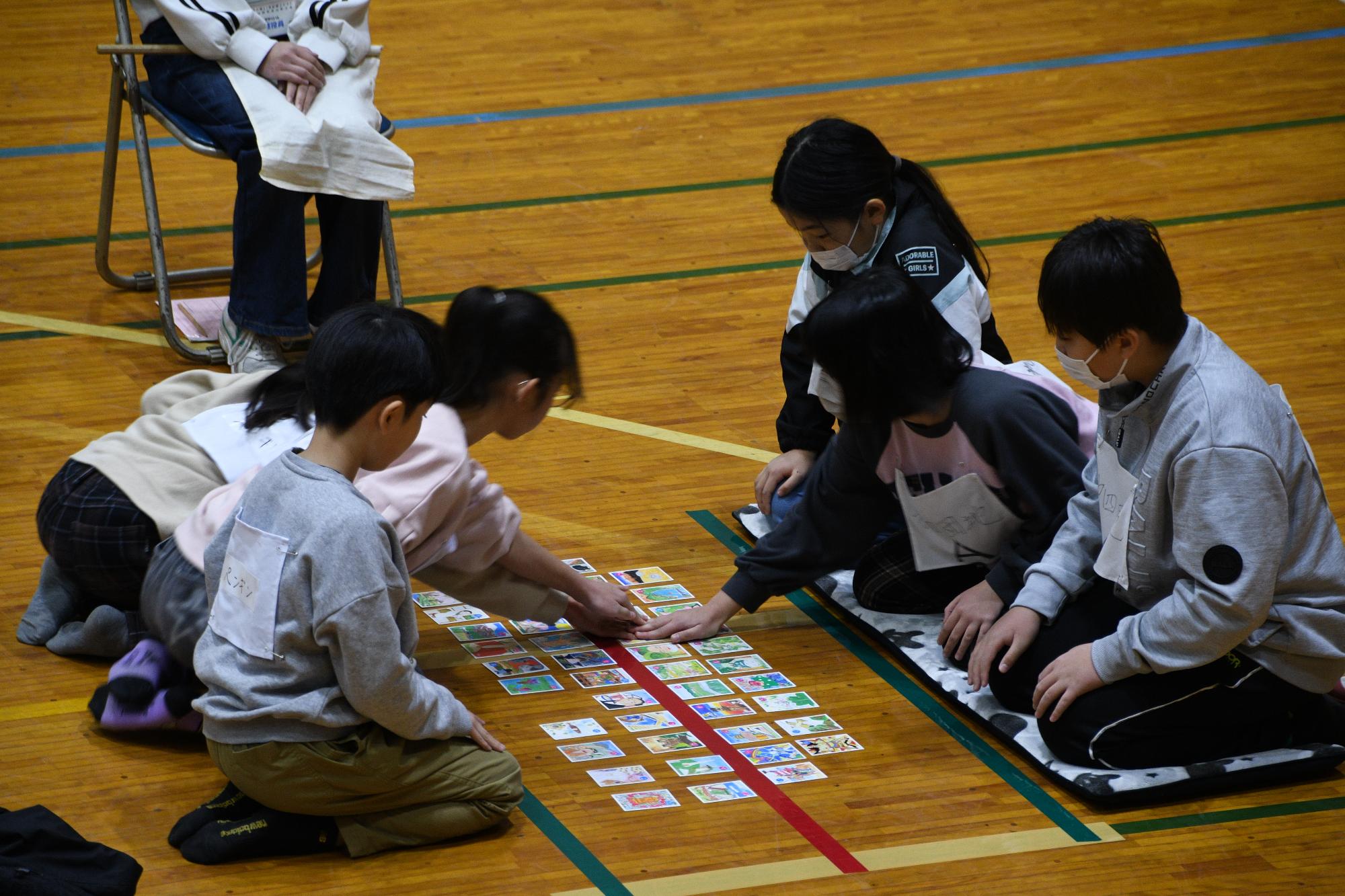 3人1組で向かい合って座る生徒がかるたをしている写真
