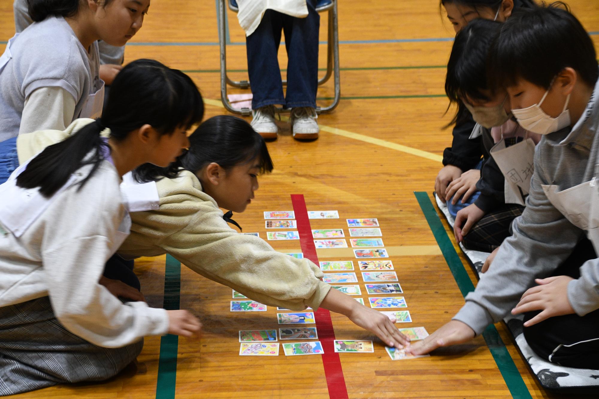 3人1組で向かい合って座る生徒がかるたをしている写真