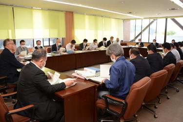 テーブルが口の字型に並べられた会議室で資料を見ながら会議が行われている写真