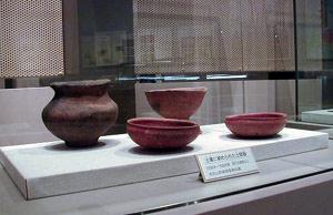 左奥に口の大きな壺型の土器、右奥に口の大きな土器、手前に2つの浅型の土器が展示されているショーケースの写真