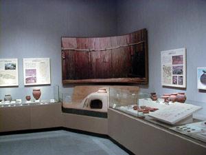 展示棚に灰色の土器(須恵器)、赤い土器(土師器)、カマドの復元模型、壁にパネルが展示されている写真