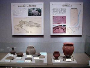 左側に灰色の土器(須恵器)、右側に赤い土器(土師器)、壁にパネルが展示されている写真