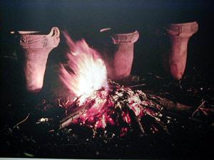 暗闇の中、焚き木が燃えて炎が出ている後ろに、3つの土器が等間隔で並んでいる写真
