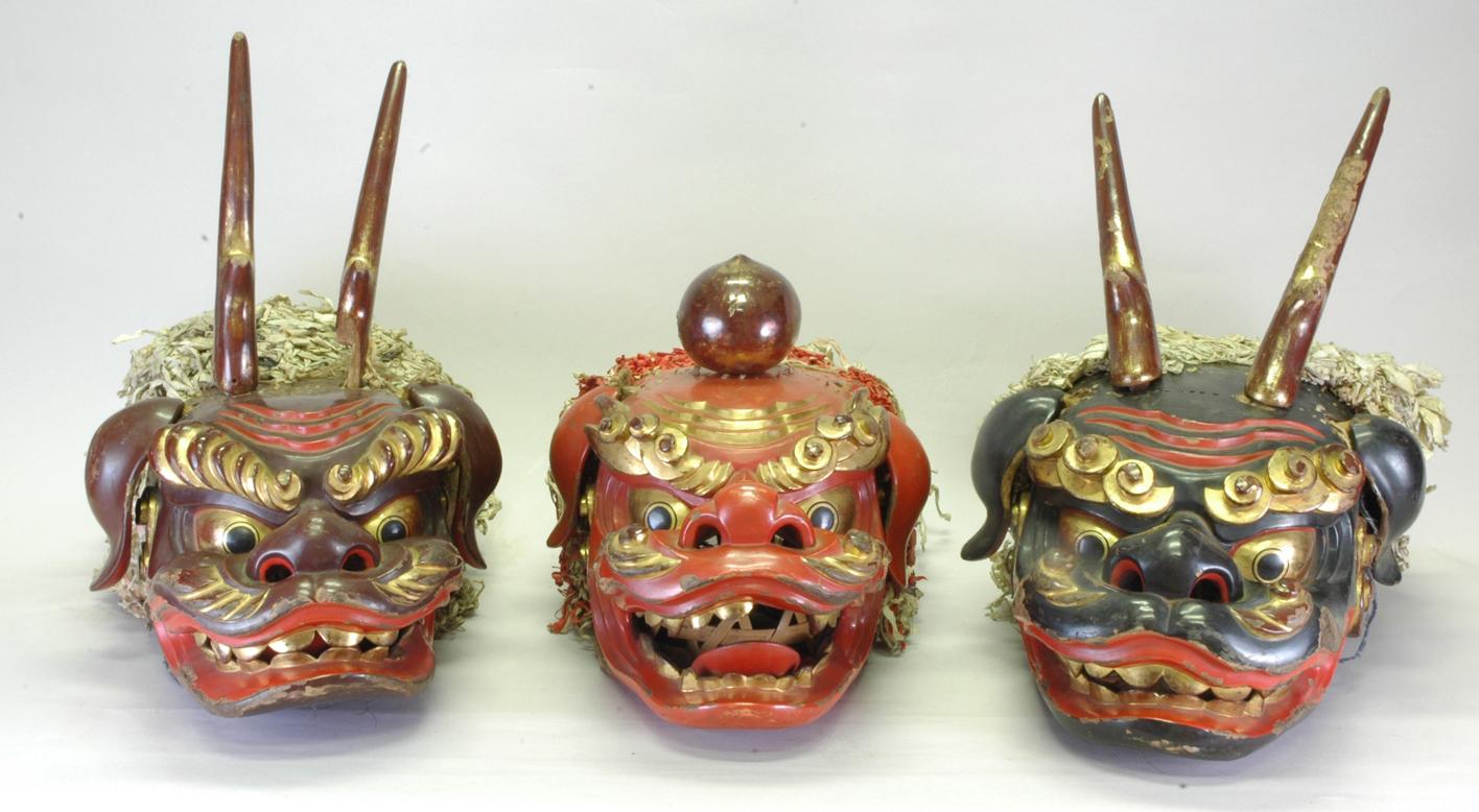 左は頭上に長い角が生えている赤色の顔、中央は玉を頭上に乗せている赤色の顔、右は頭上に長い角が生えている黒色の顔の獅子頭が並んでいる写真