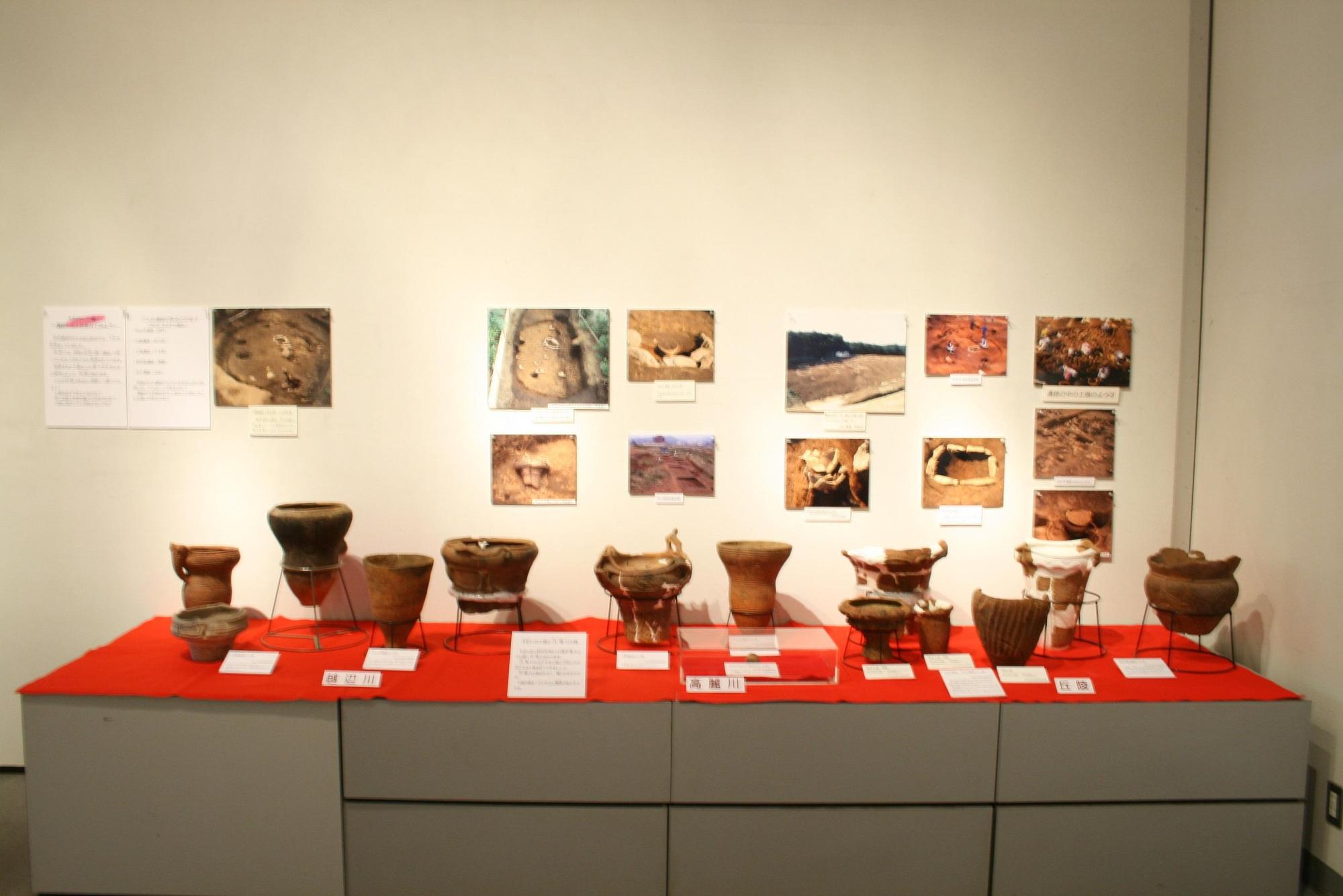 奥の壁に発掘場所などの写真、手前の台に様々な形の縄文土器が展示されている写真