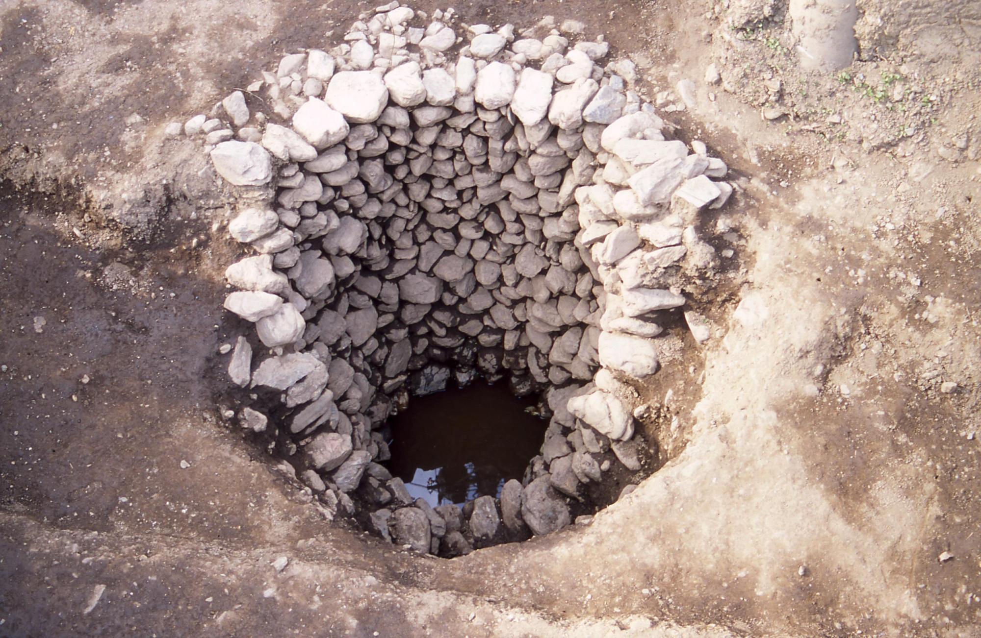 穴の奥から周りを囲むように石が沢山積み上げられている石組みの井戸跡の写真