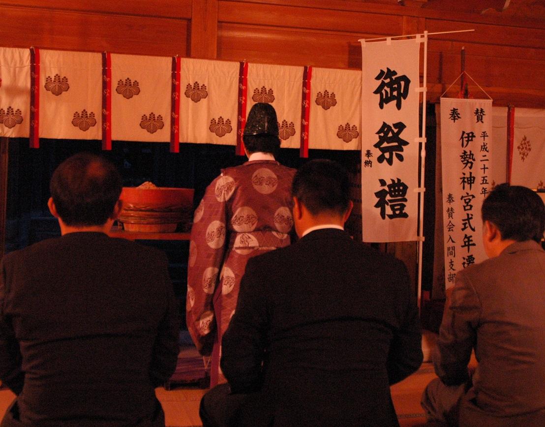 3名のスーツ姿の男性が横に並んで座り、宮司によるお祓いを受けている様子の後ろ姿の写真