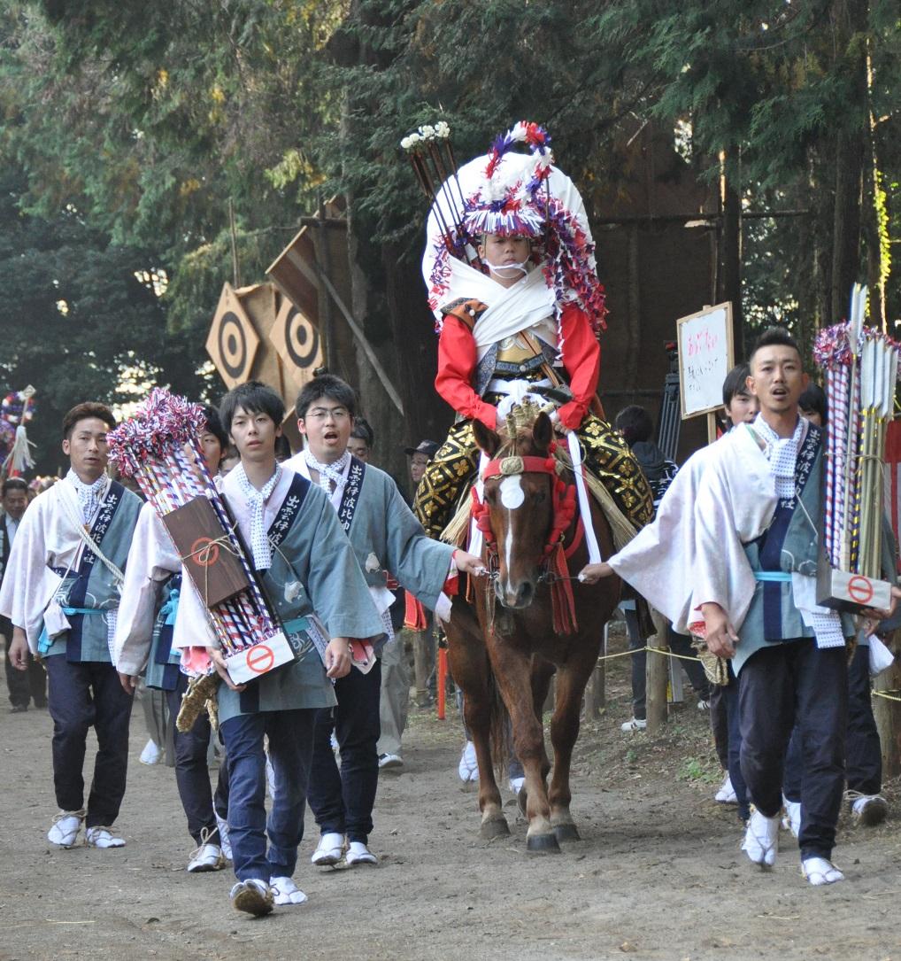 馬に乗った正装姿で花笠を被った乗り子の周囲を歩く口取り衆が、矢を持ち馬の紐を引き、掛け声を出しながら登場している写真