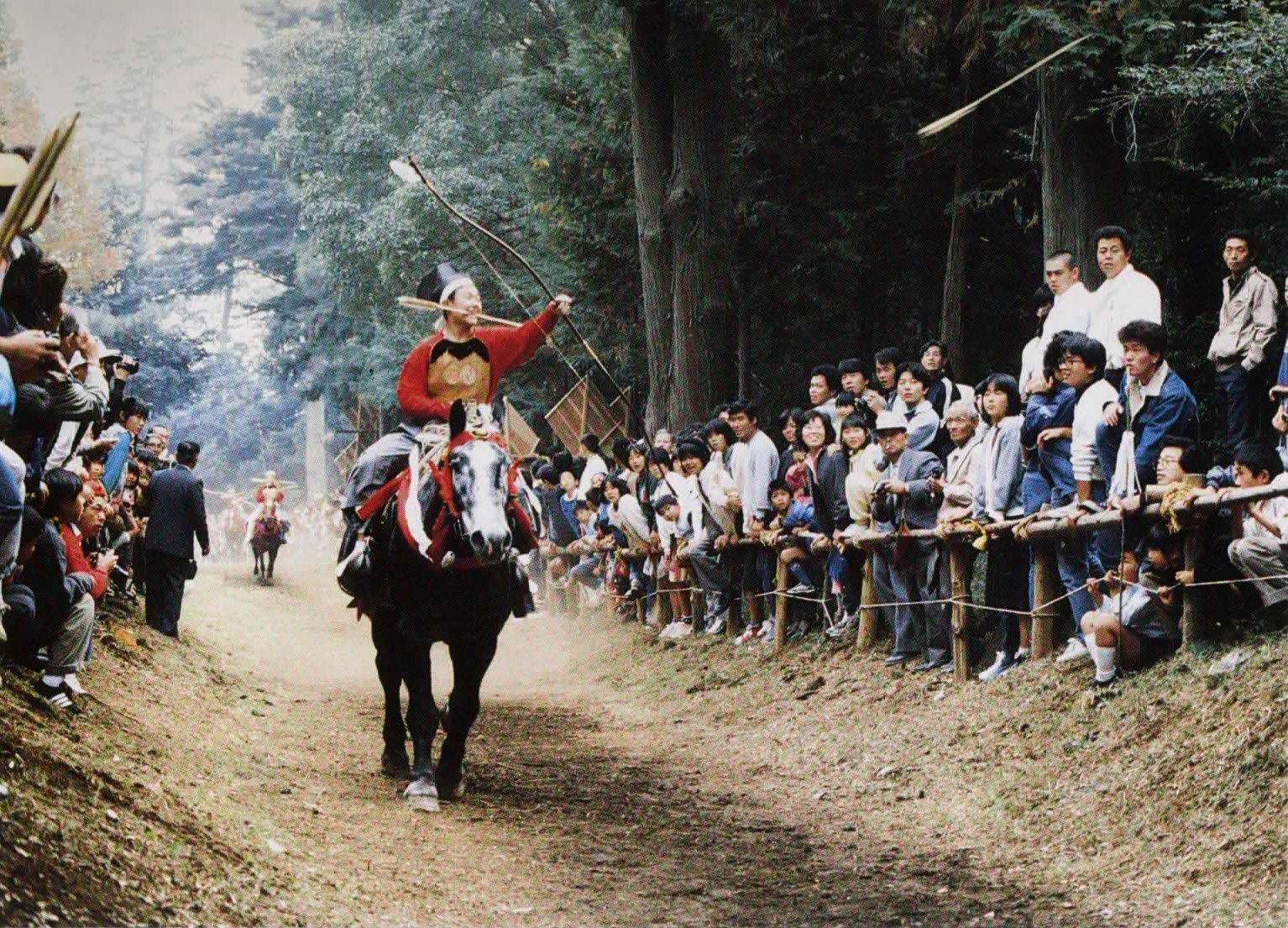 流鏑馬の衣装を身にまとった男性が走っている馬に乗り、観客が見守るなか的に向かって矢を射ている様子の写真