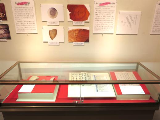 壁に土器に記された古代の文字や説明書き、ショーケースの中に江戸時代や明治時代に書かれた手紙などが展示されている写真