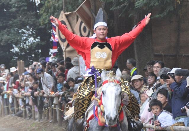 走っている白馬にまたがった烏帽子をかぶった乗り子が、両手を広げている馬上芸の写真