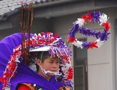 流鏑馬の衣装を身にまとった男性の頭上周りに赤や白、紫色で彩った花笠や馬印の写真