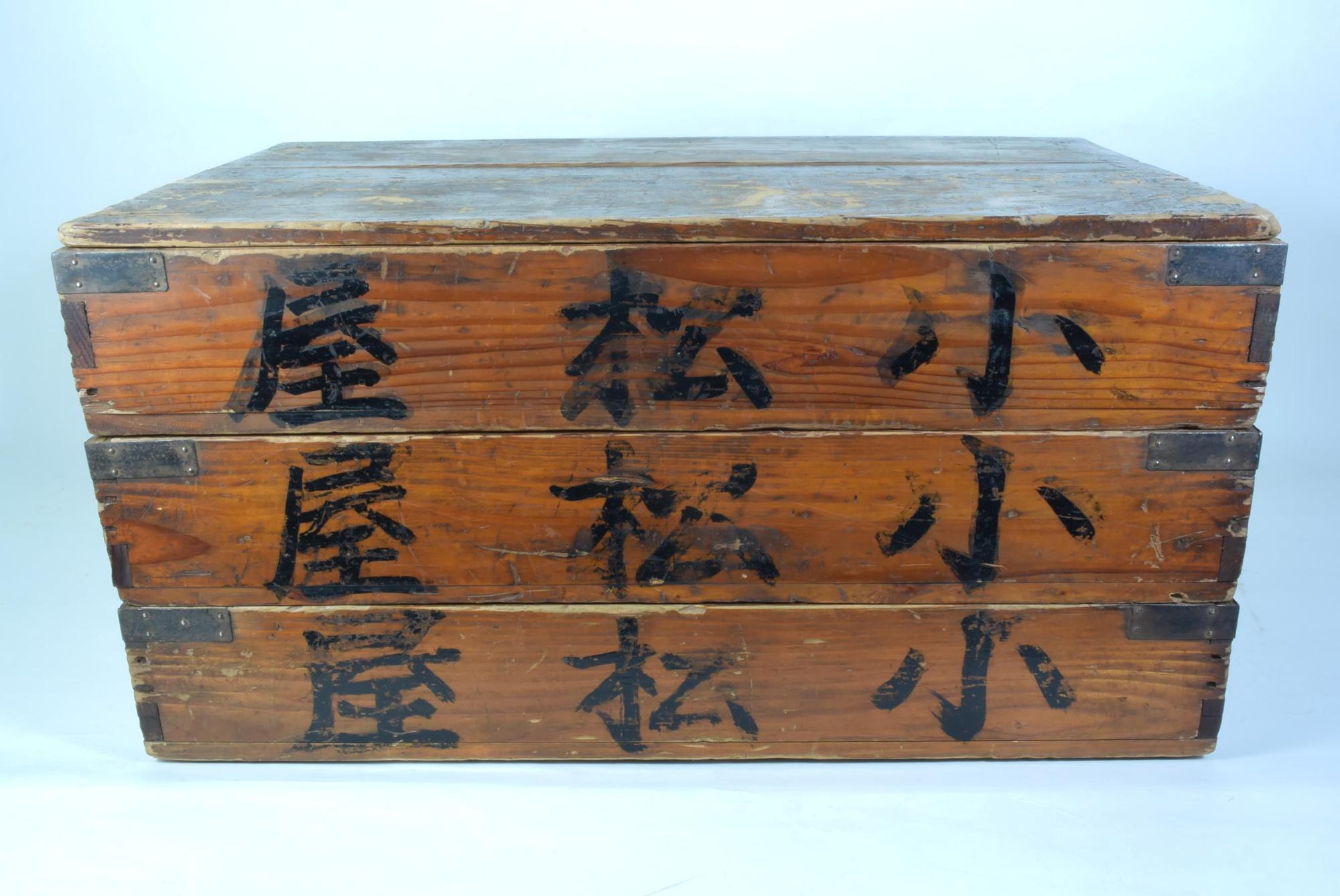 木箱の側面に「小松屋」の文字が書かれており長方形の木箱が3段積み重ねられ、蓋がされている菓子箱の写真