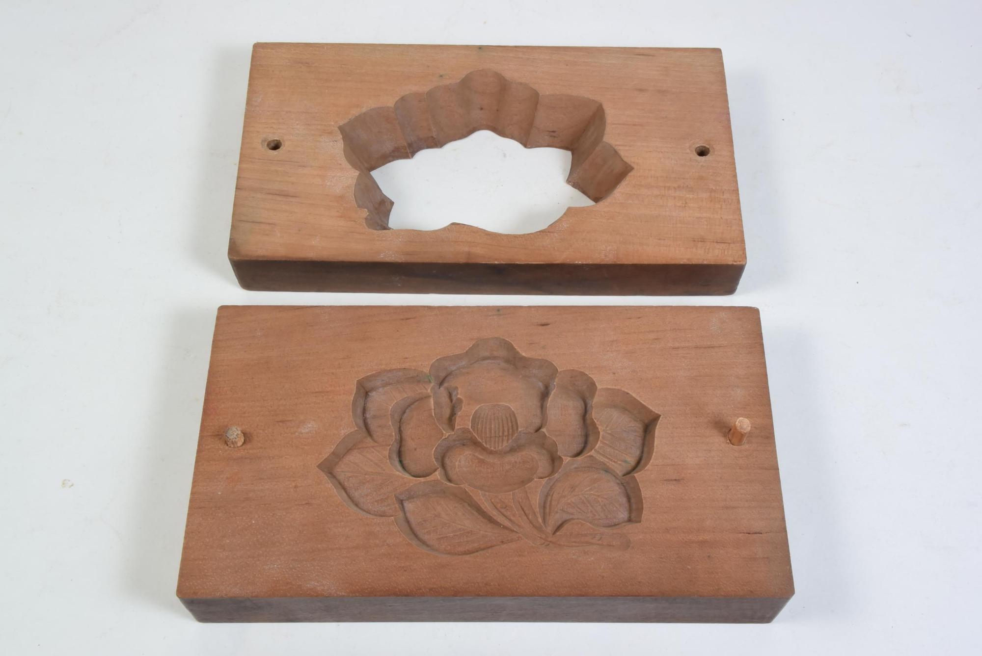 1枚はつばきの花の形に板をくり抜いた型、もう1枚は椿の花の形が掘ってある板が並べて置いてあるツバキの花の打菓子の型の写真