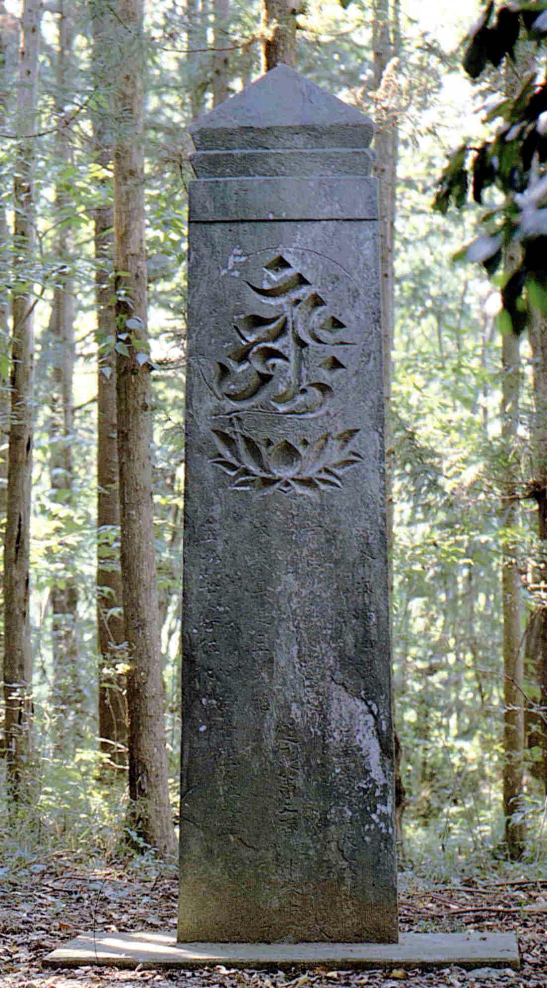木々の生えた林の中にある高さが3メートル延慶の板碑の写真