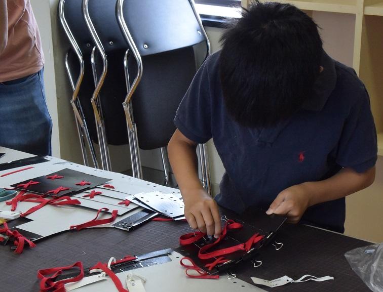 参加した小学生が黒の甲冑のパーツの穴に赤い紐を通している写真