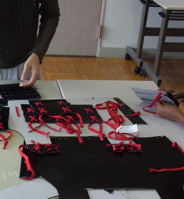 机の上に組み立てる前の赤い紐が通された甲冑のパーツが置かれている写真