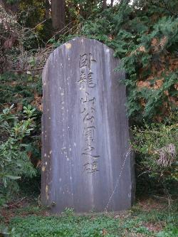 緑に囲まれた場所に建てられている「臥龍山公園之碑」の文字が刻まれている石碑の写真