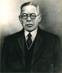 黒縁の丸眼鏡をかけ、スーツ姿の栗原勘次郎の肖像画