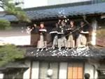 的宿の屋根から袴姿の男性たちが餅まきをしている写真