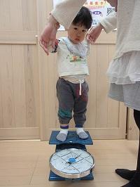 両手を支えらえて体重計に乗っている小さな男の子の写真