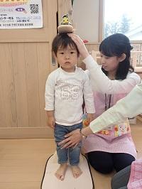 身長計に背筋を伸ばして立っている男の子と、はかりの数字に目を向けている保健師さんの写真