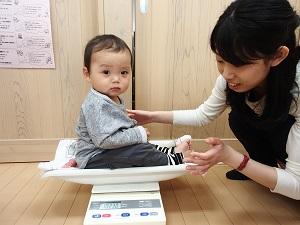 ベビー用体重計に座っている男の子とはかりの数字に目を向けている保健師さんの写真