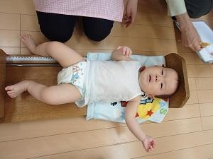乳児用ベッド型身長計に寝かされ、泣き出してしまっている赤ちゃんの写真