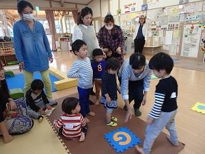 「G]と書かれたカードが床に置かれており、その周りに子ども達と大人の方が集まって、一人の女性がカードに手を伸ばそうとしている写真