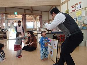 ポール先生と向かい合って立っている男の子と女の子、床に座っているサラ先生、その様子を見ている保育士の写真