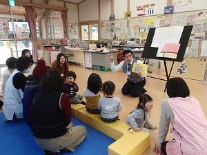絵本の読み聞かせをしているポール先生、座って読み聞かせを聞いている親子の写真