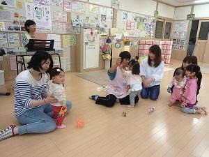 ピアノを演奏している前で遊ぶ子供と母親、職員の方々の写真