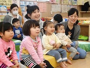 母親たちと一緒にパネルシアターを見ている子供たちの写真