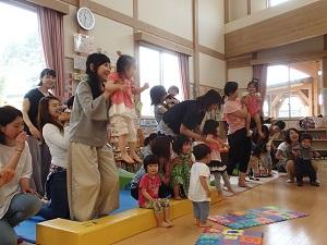 立ち上がって子供を抱き上げている母親、座っている子ども、立っている子どもの写真