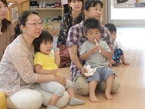 参加者の親子が前方をみながら、お母さんの膝に座った子ども達が歯ブラシを手に持って歯を磨いている写真