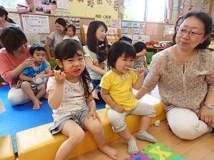 黄色いブロックに座っている女の子2人がそれぞれ歯ブラシを持って歯を磨いている様子を横に座っている女性が見守っている写真