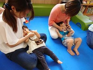 小さな男の子と女の子がお母さんの膝の上に子どもの頭を乗せて、仕上げ磨きをしている様子の写真