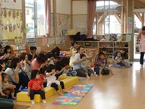 子どもの遊びスペースに参加した親子が座りみんなで、両手の人差し指と真ん中の指を伸ばした同じポーズをしている写真