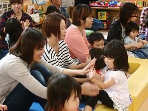 子どもの遊びスペースに参加した親子が向かい合って座り、両手の手のひらを合わせている写真