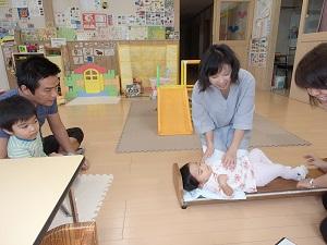 お父さんとお兄ちゃんが見守る中お母さんが赤ちゃんを寝転ばせながら身長を測っている写真