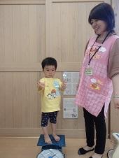 保健師さんの横のはかりのような体重計に真面目な表情でたっている男の子の写真