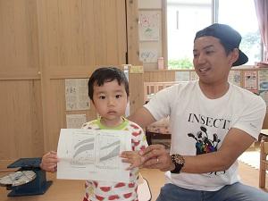 用紙をみせる男の子と自慢そうなお父さんの写真