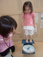 はかりのような体重計に乗っている女の子と保母さんが数値を覗き込んでいる写真