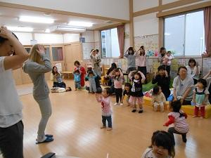 両手を頭の上にのせてリズム遊びをしているフリーダ先生と親子の写真