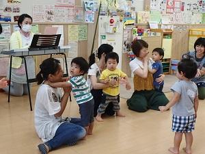 エレクトーンの後ろで膝をついて座っている女性スタッフの前で、3組の親子が座り、右側のエプロンを着用した女性スタッフが話しをしている写真