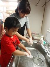 赤い服の男の子とその母親が一緒に手を洗っている写真
