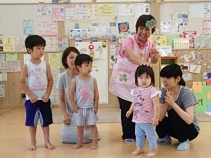 左側に2名の男の子が立ち後ろに座った母親、右側にお揃いのボーダー柄の服を着た座っている母親と前に立つ女の子、母親の左隣に立つピンク色のエプロンを着用した女性スタッフが女の子の頭に左手を置いている写真