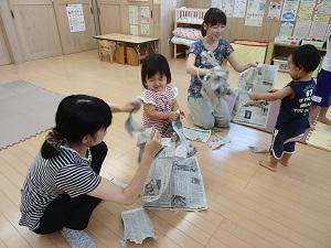 子供と一緒に母親が、楽しそうに新聞紙をビリビリに破いている2組の親子の写真