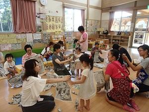 床に座っている参加した母親たちが、子供たちと一緒に新聞紙をビリビリに破いている写真